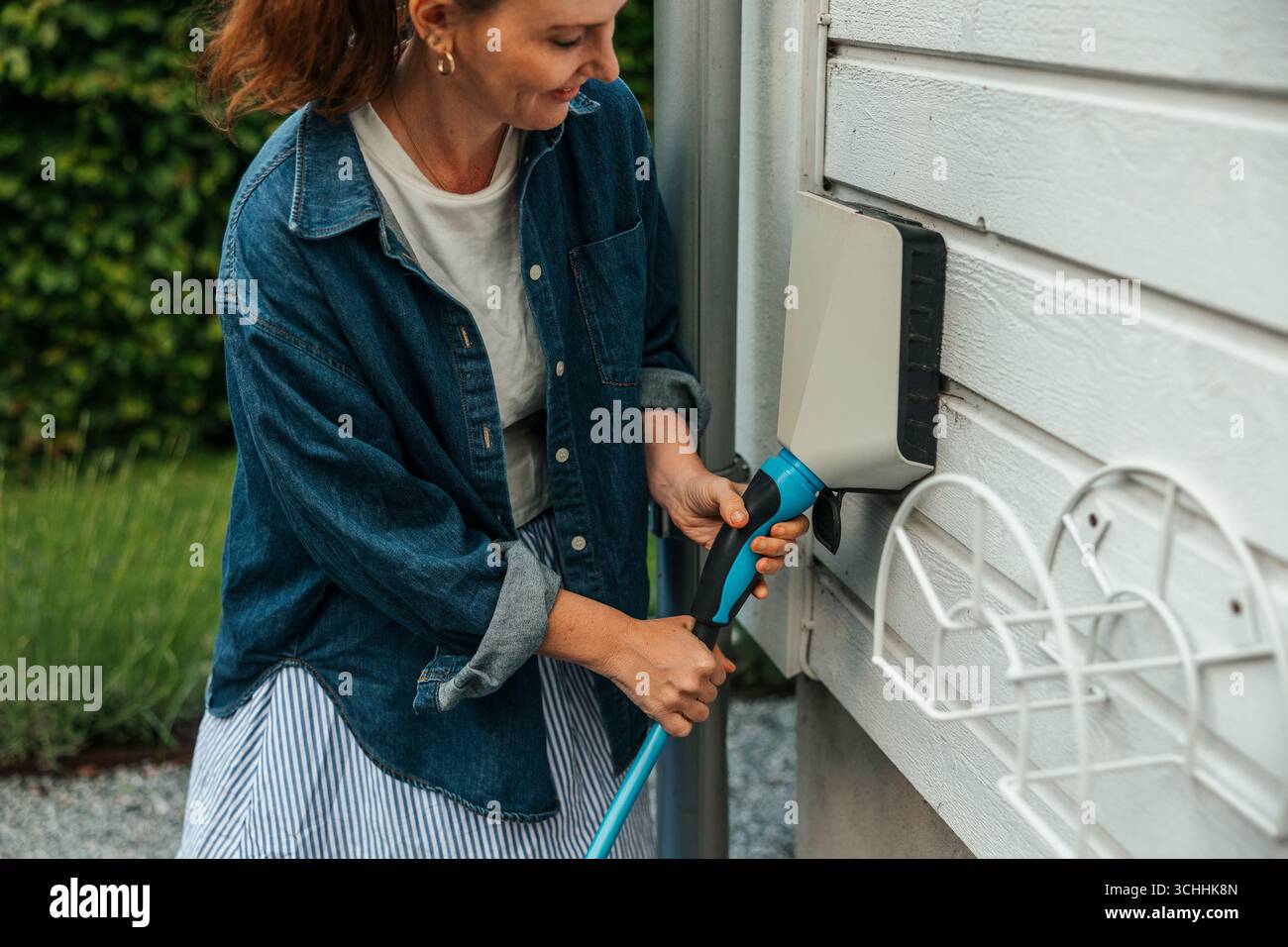 Smiling woman plugging electric plug in outlet on outside wall in back yard Stock Photo