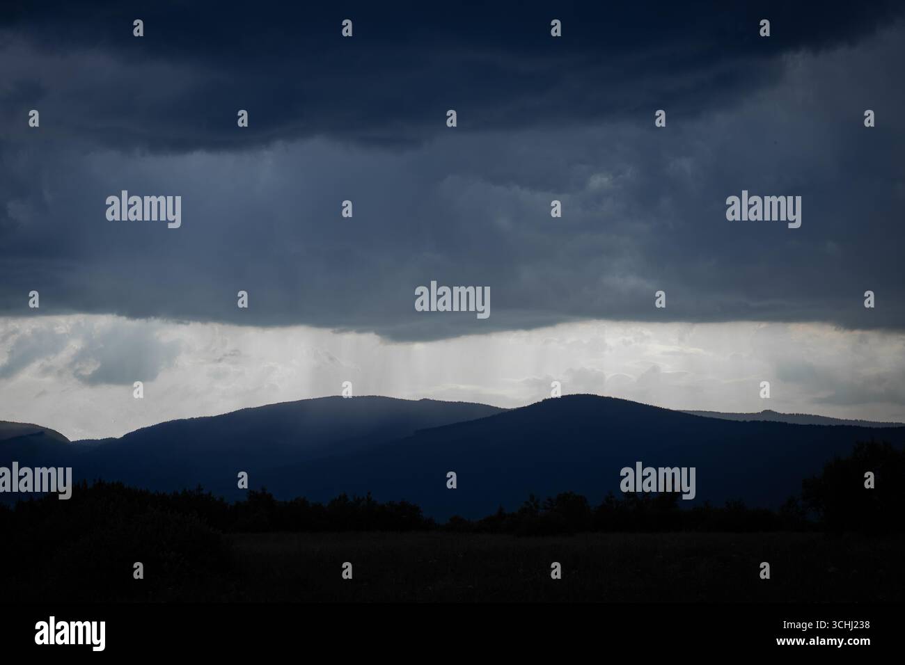 Dark storm clouds gather above silhouetted mountain peaks, while a ...