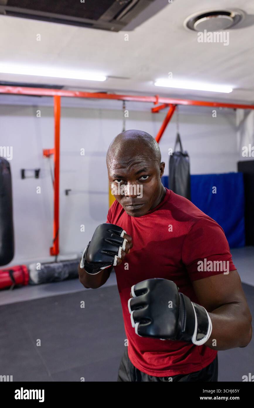 African american man standing in martial arts gym wearing training gloves next to punching bag Stock Photo