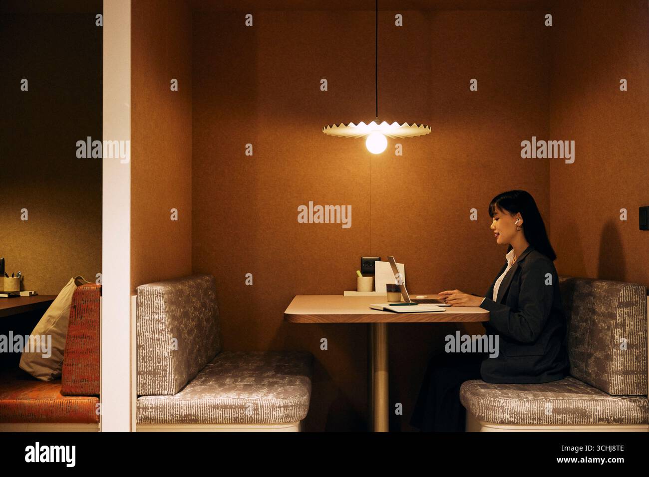 Side view of female business entrepreneur talking on video call through laptop while sitting on sofa at illuminated cowo Stock Photo