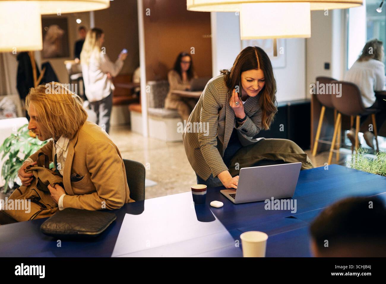 Female business professional talking on smart phone while using laptop on table in coworking office Stock Photo