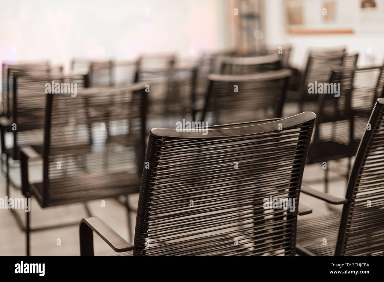 Multiple black chairs are neatly arranged in rows within a bright, modern conference room, waiting for attendees to arrive for an upcoming meeting or Stock Photo
