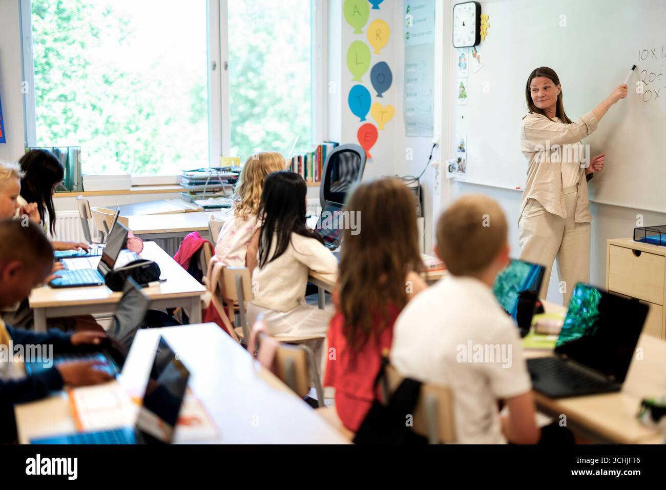 Female teacher explaining students over whiteboard at elementary school Stock Photo