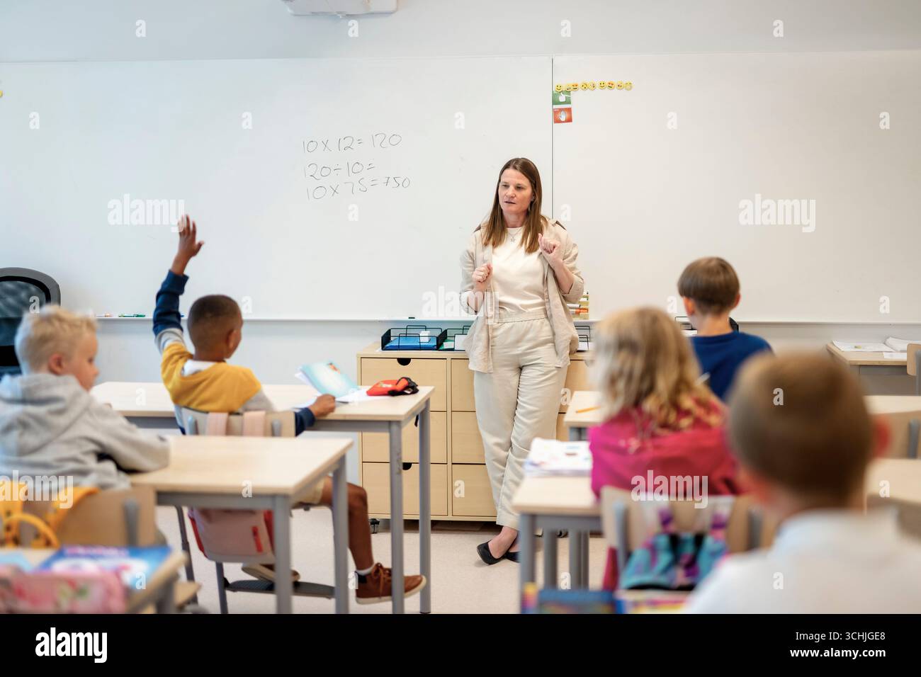 Female teacher teaching mathematics to group of elementary students sitting at desk in classroom Stock Photo