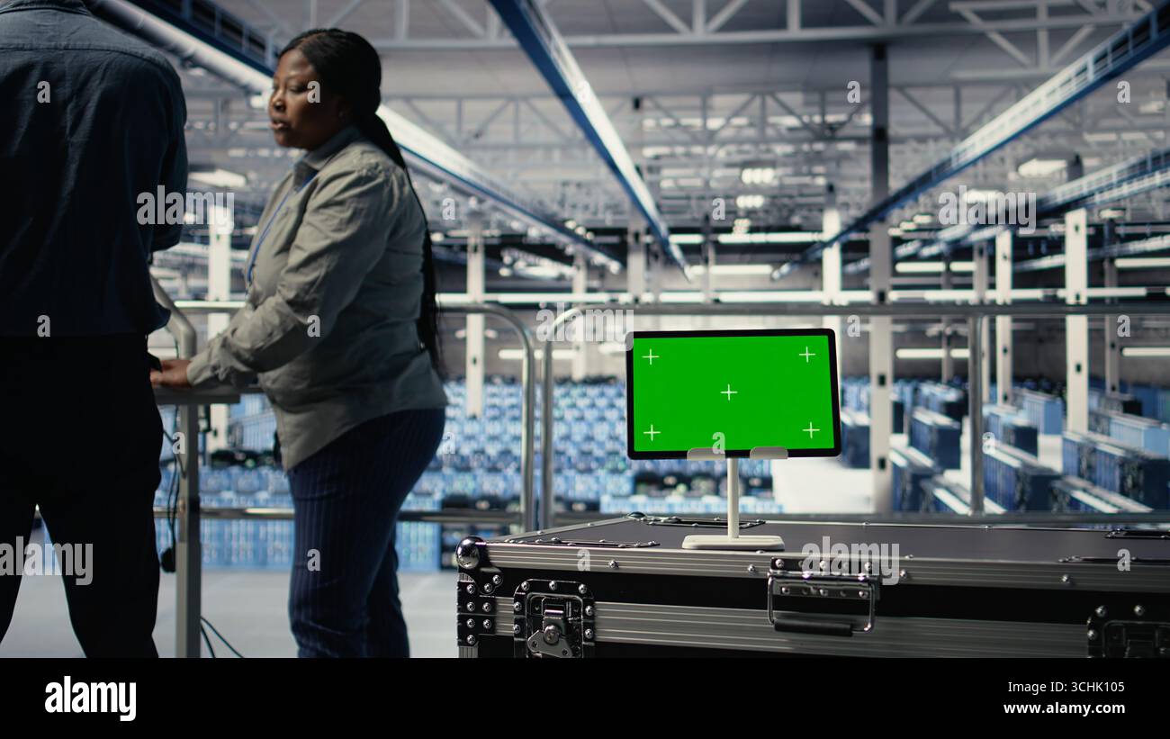 Data center IT professionals check AI dashboard using isolated screen tablet. Server room developers test artificial intelligence tools on chroma key device to ensure reliable performance, camera A Stock Photo