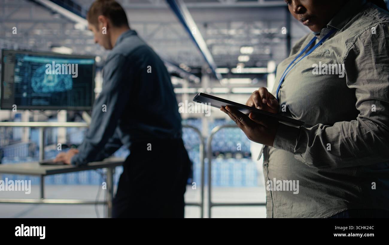 Data center programmers check AI dashboard using tablet, doing systems review. Server hub coworkers test artificial intelligence tools on device to ensure reliable performance, camera A Stock Photo