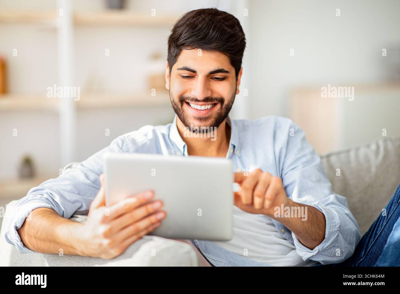 Happy arab man using digital tablet, shopping online, browsing internet or working remotely on tab computer Stock Photo