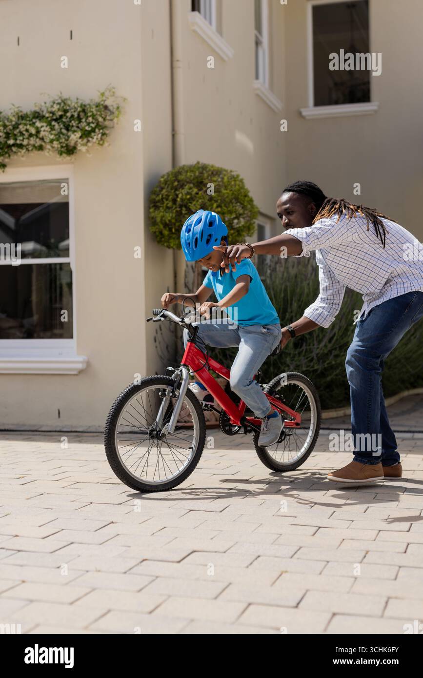 Father teaching son to ride bicycle outside home, encouraging and supporting him Stock Photo