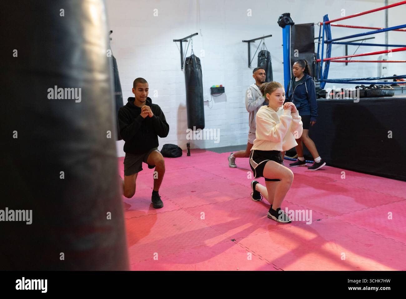 Diverse fitness group performing forward lunges on mats at boxing gym ...