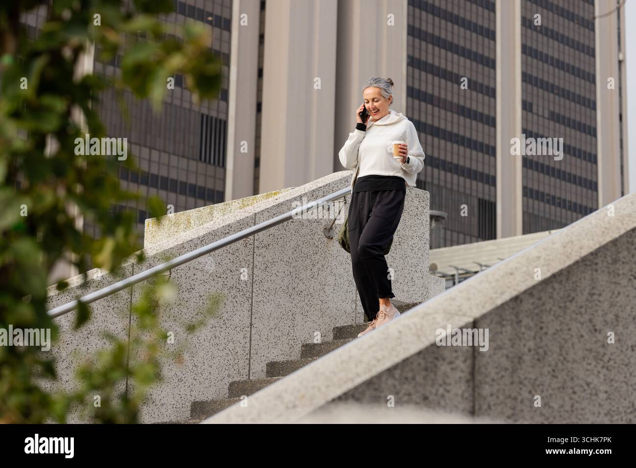 Woman descending stairs at office talking on smartphone, coffee cup, crossbody bag, copy space Stock Photo