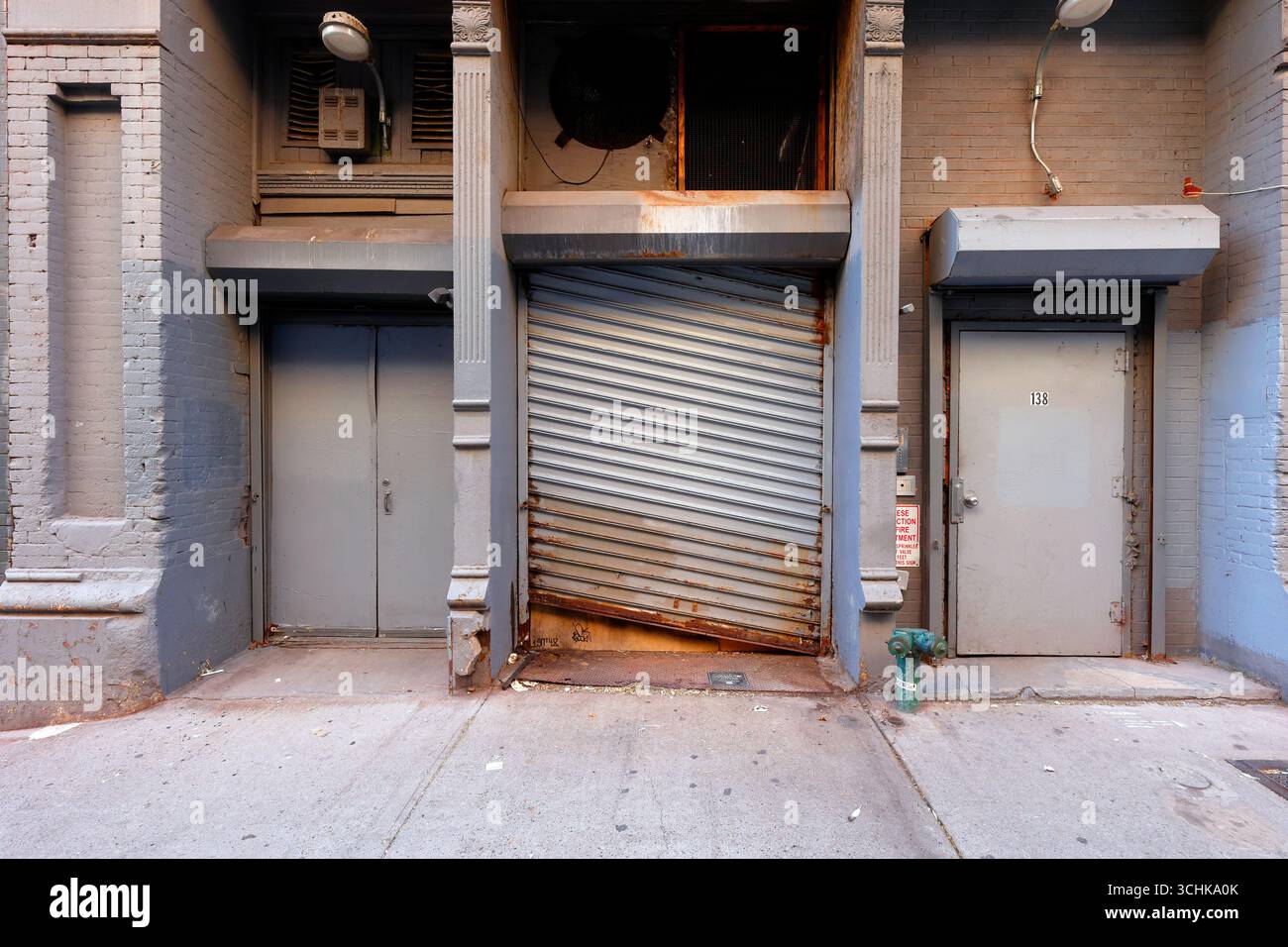 Two doors and a rolldown gate painted gray in a brick building in New York City Stock Photo