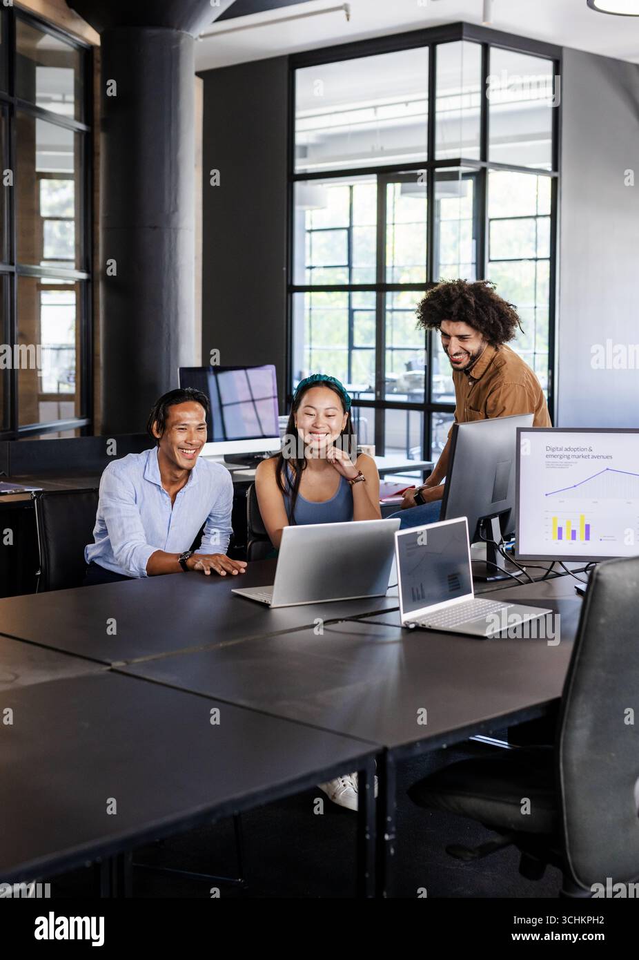 Diverse team collaborating on laptops in modern office, discussing digital analytics Stock Photo