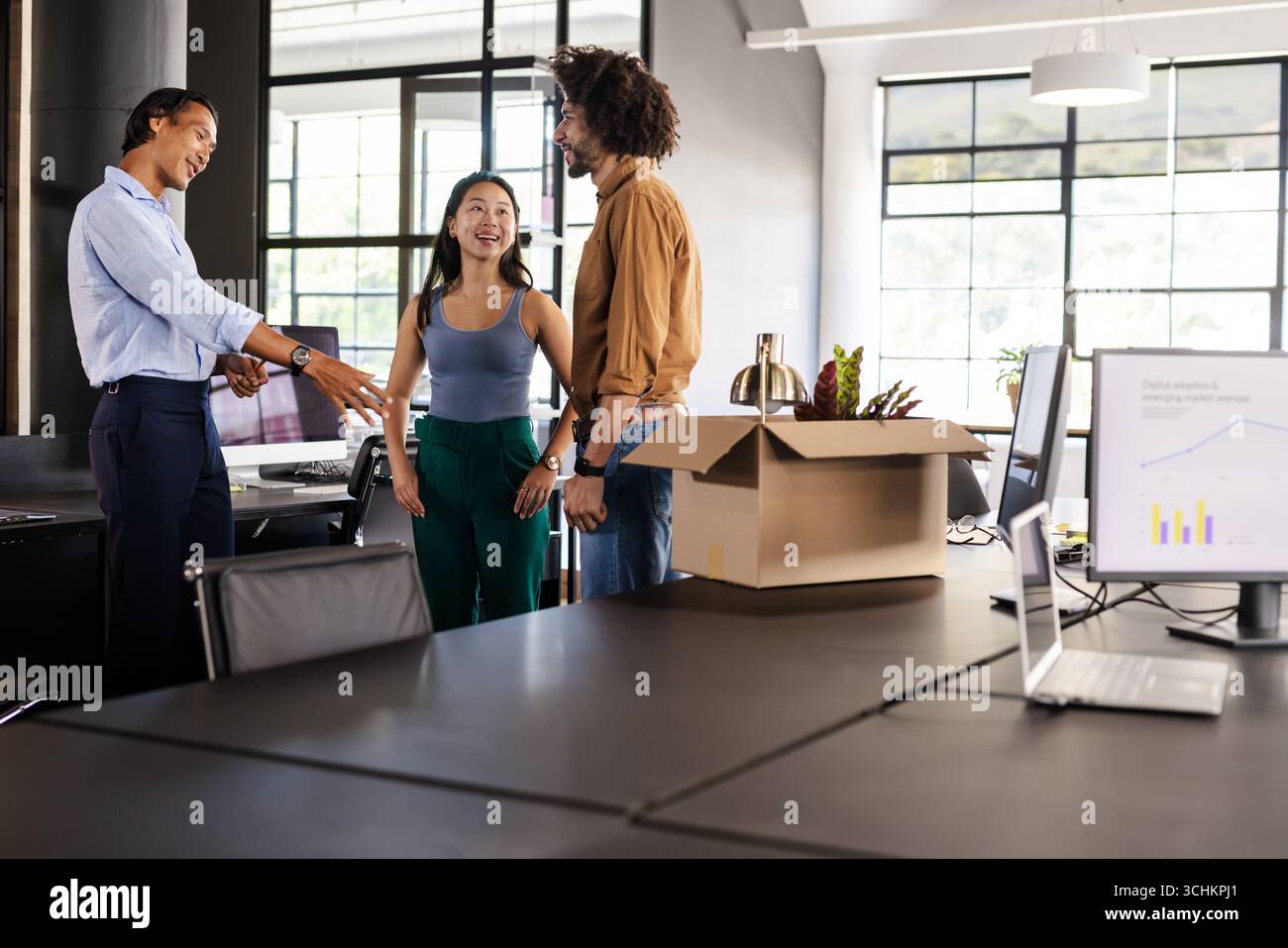 Diverse colleagues discussing project in modern office with charts on computer screens Stock Photo