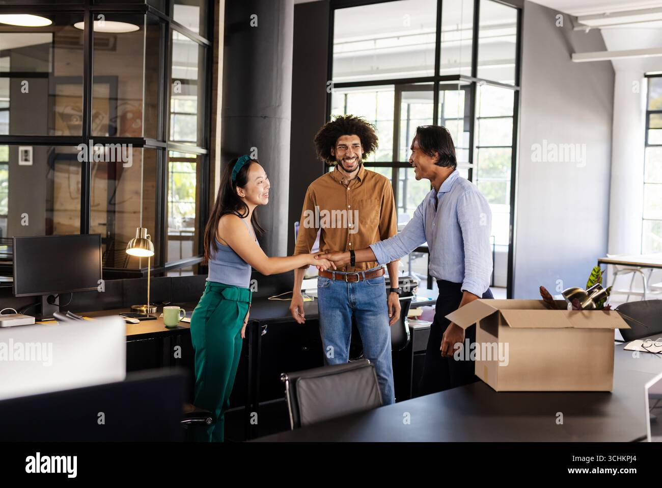 Diverse colleagues greeting each other in modern office, smiling and shaking hands Stock Photo
