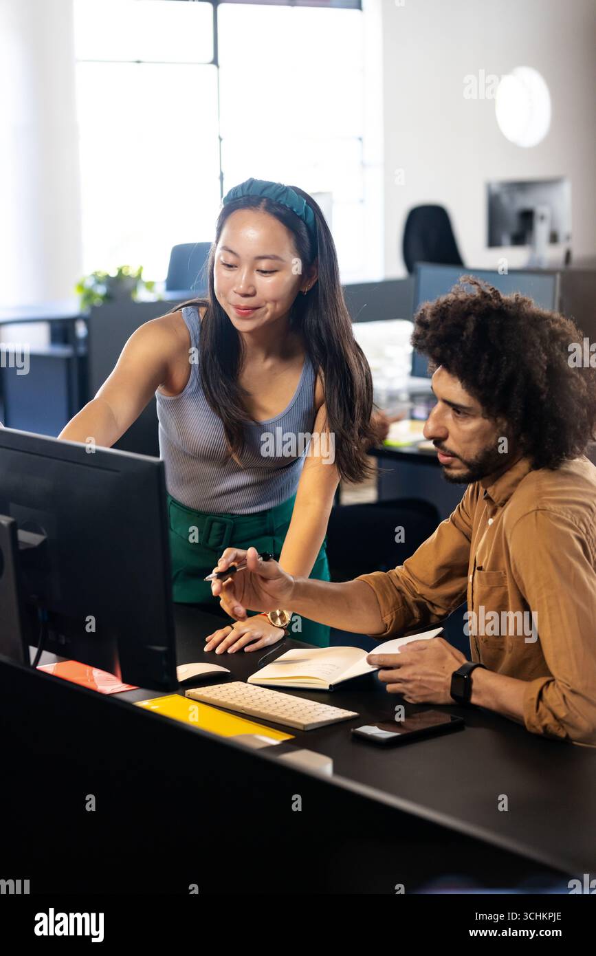 Diverse colleagues collaborating at office, discussing project details on computer screen Stock Photo