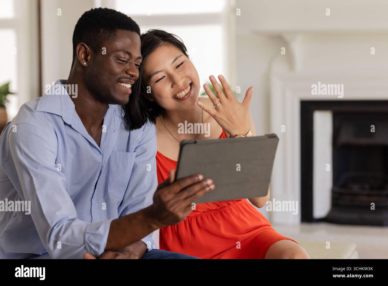 Happy couple video chatting, showing engagement ring, sitting together at home Stock Photo