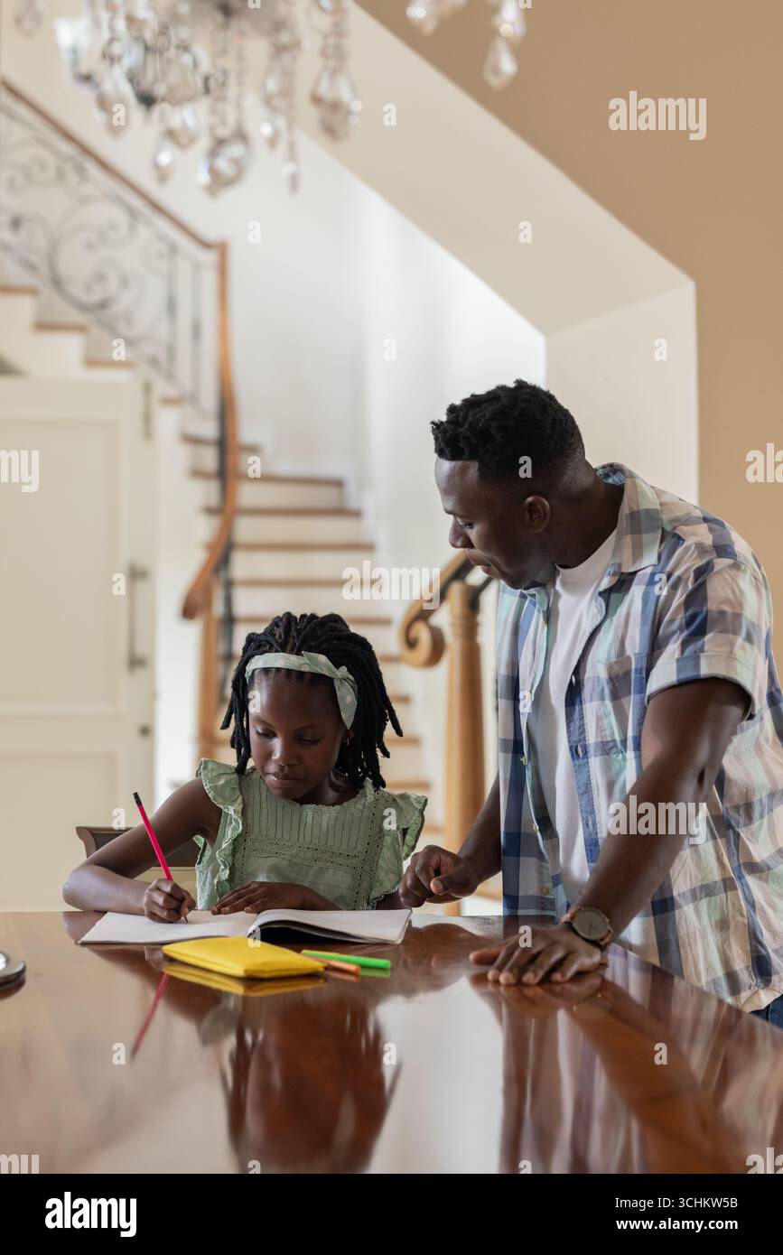 African American father helping daughter with homework at home, both concentrating Stock Photo