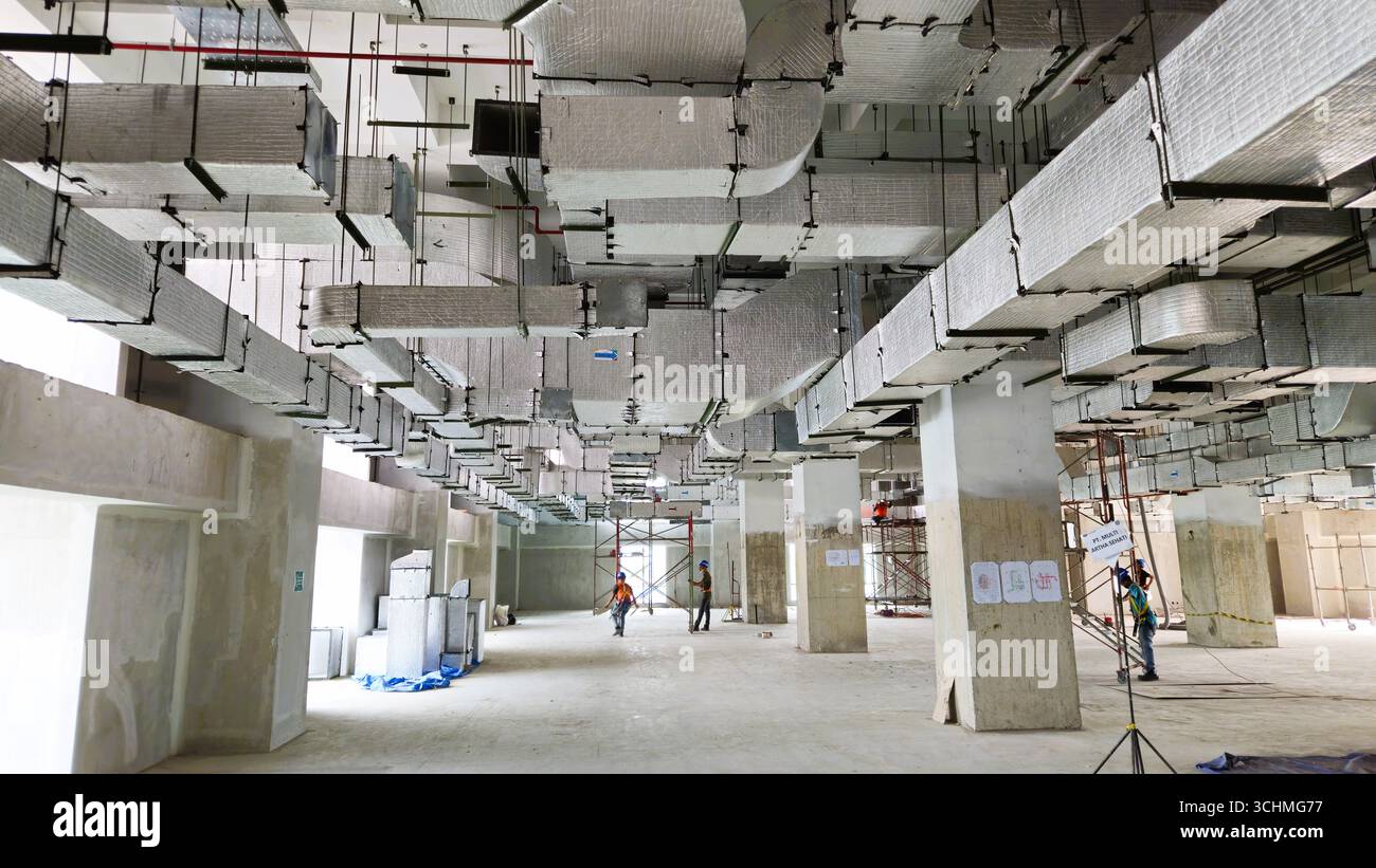 Construction workers inside unfinished building with exposed ducts and concrete pillars. Bandung, Indonesia. November 30th, 2023 - Smartphone Captured Stock Image