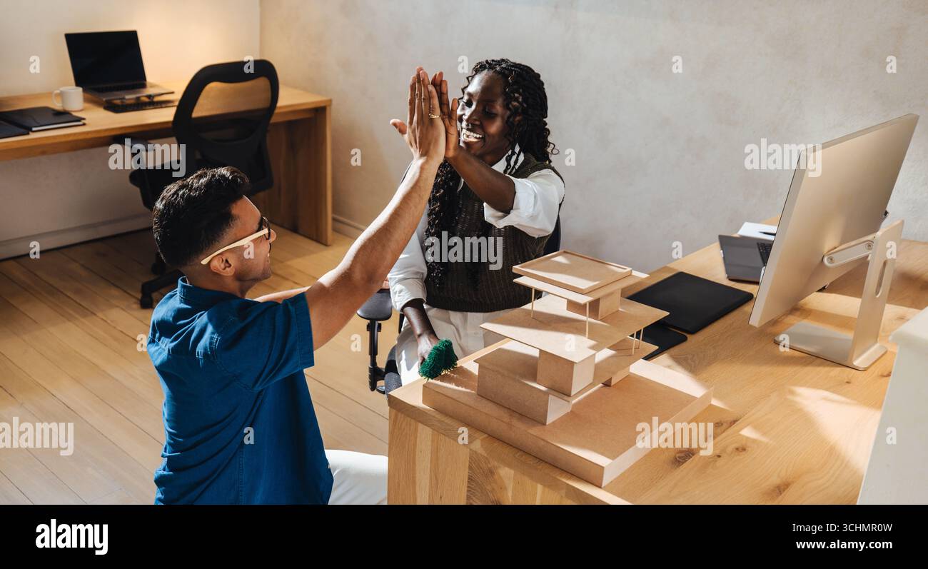 Two colleagues exchange a high-five while discussing architecture in a modern workspace. Stock Photo