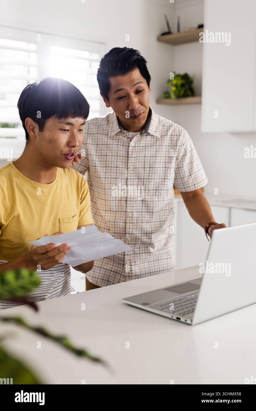 Asian father and son reviewing documents together at home using laptop Stock Photo