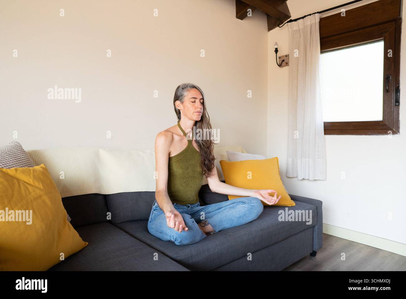 Serene woman practicing mindfulness meditation on her sofa, embracing tranquility and self-care in the comfort of her living room Stock Photo