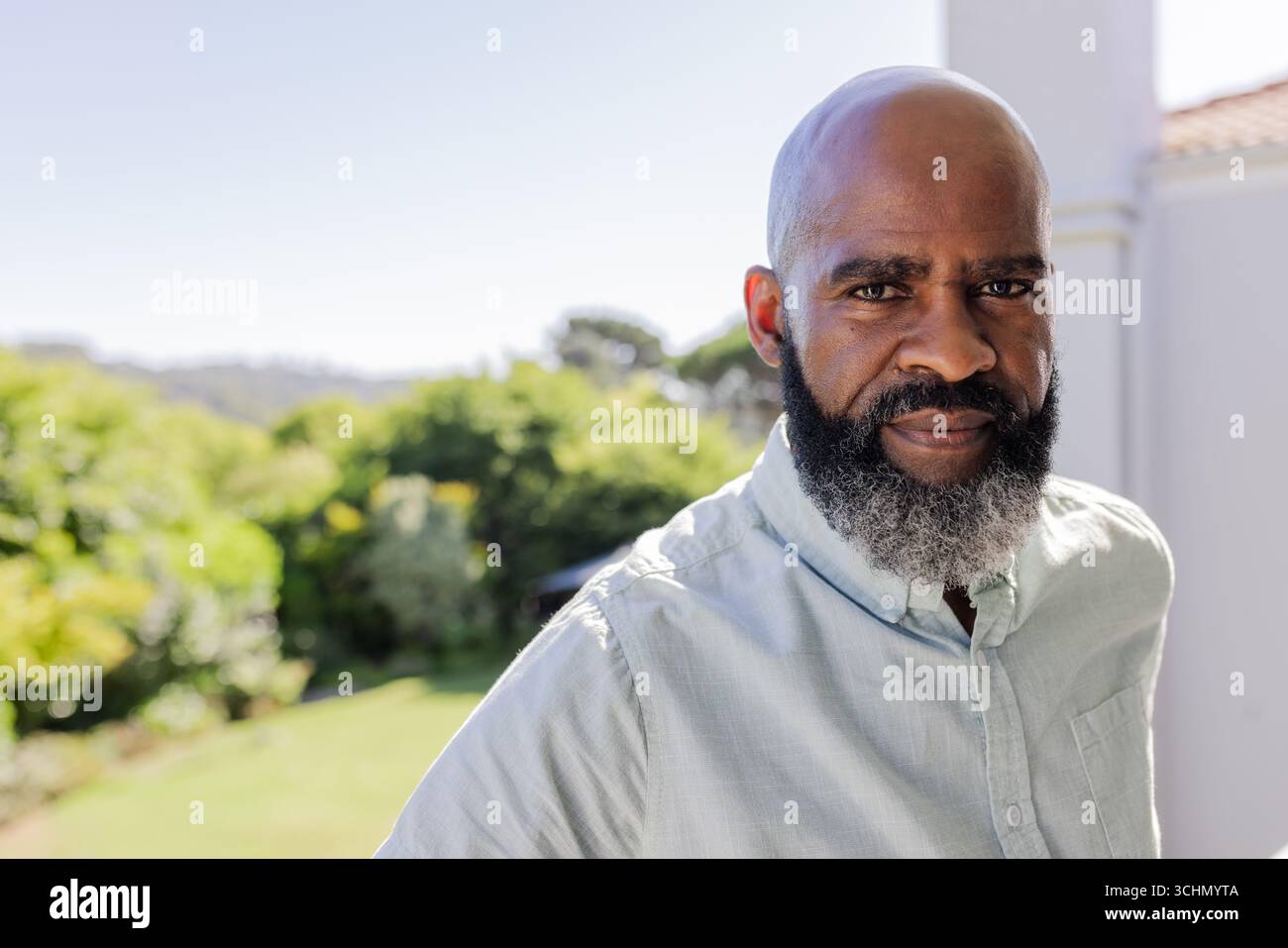 African American man standing outdoors, looking thoughtful in sunny garden setting Stock Photo