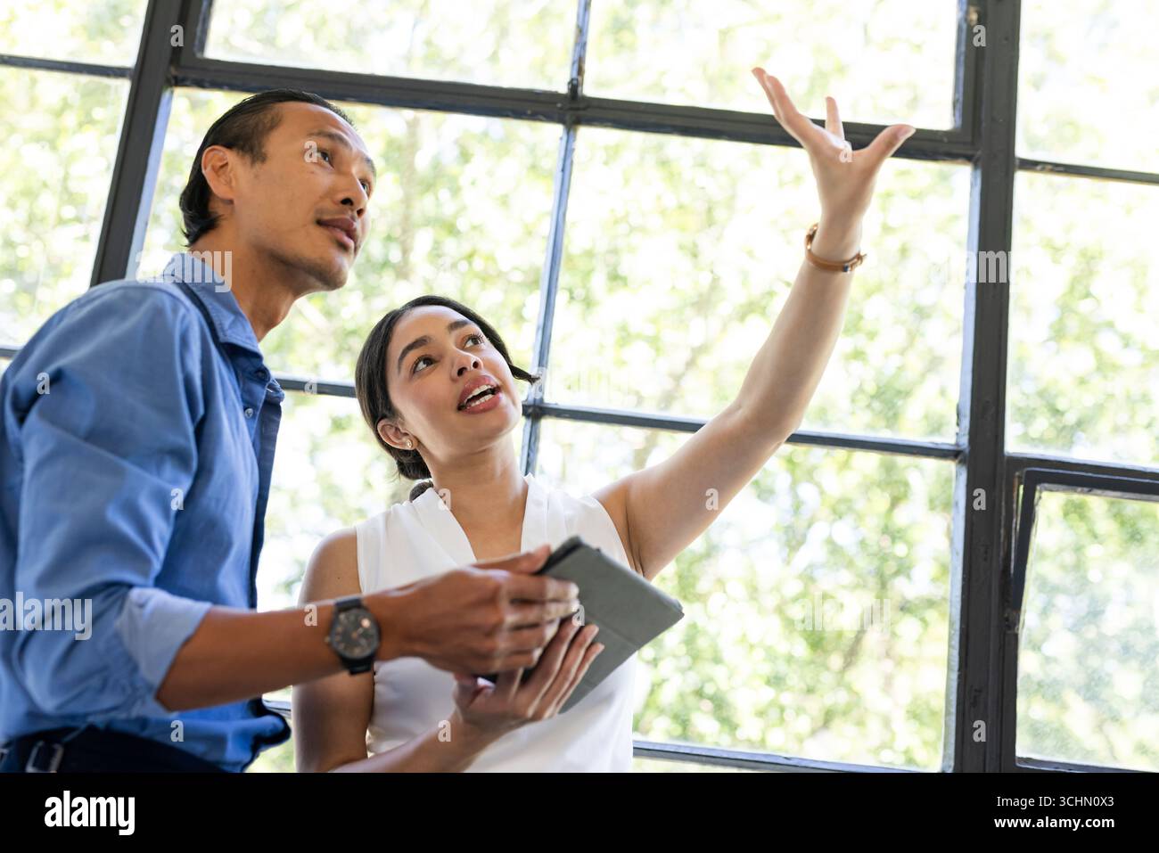 Diverse colleagues discussing project details while using tablet near large office window Stock Photo