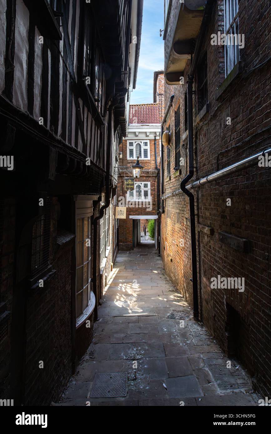 A charming narrow alleyway in York, England, flanked by timber framed and brick buildings, with stone paving leading toward a quiet courtyard. Stock Photo