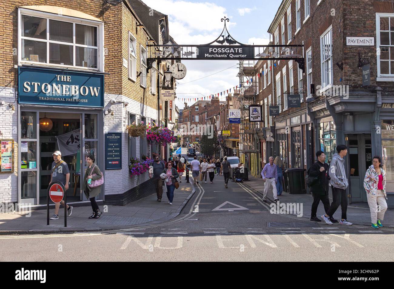 Tourists and locals on Fossgate Merchants Quarter, a historic shopping street with independent shops, hanging baskets, and lively atmosphere. Stock Photo