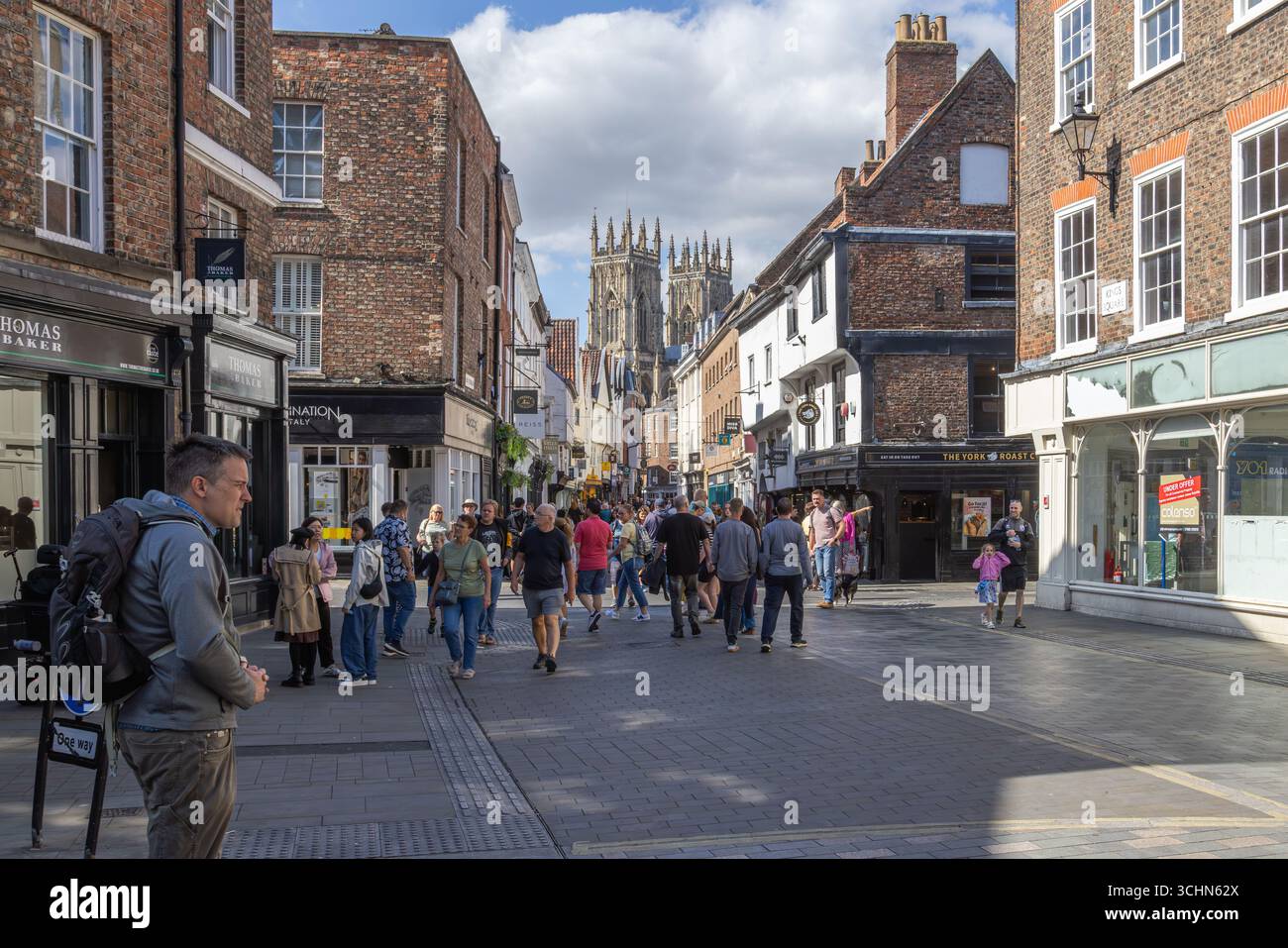 Tourists and shoppers on a busy pedestrian street in York, England, with historic buildings, retail shops, and York Minster in the background. Stock Photo