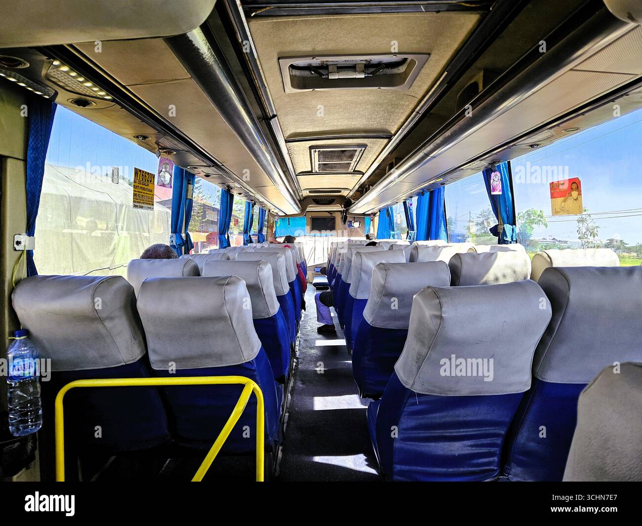 Empty interior of modern tour bus with rows of blue passenger seats in daylight. Solo, Indonesia - December 16th, 2023 - Smartphone Captured Stock Image