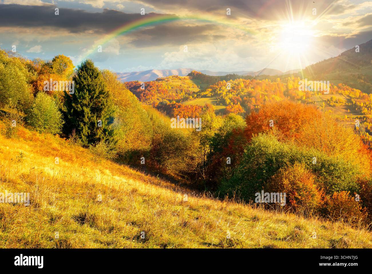 autumn mountain landscape at sunset. beautiful countryside in highlands with rural fields and colorful deciduous trees. rolling hills inder the rainbo Stock Photo