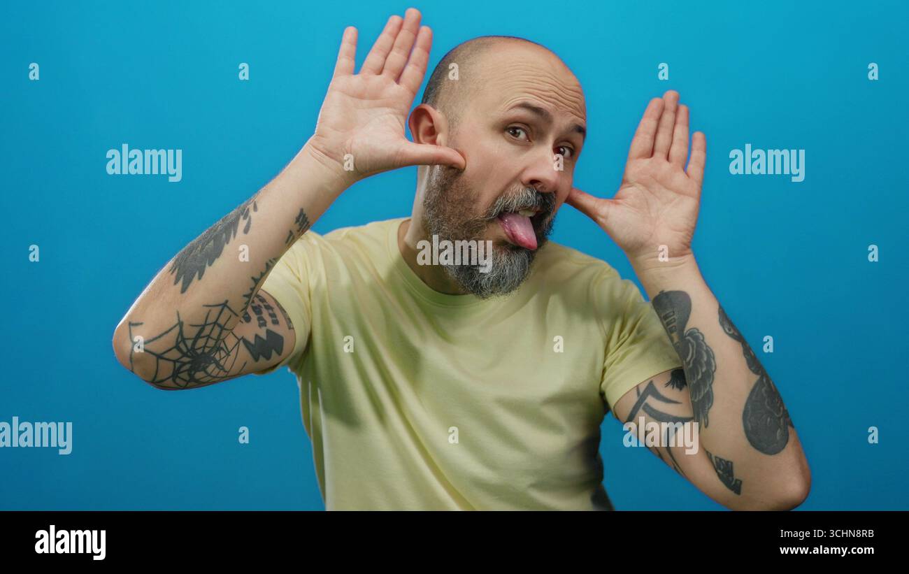 Man posing playfully with tattoos and beard against bright blue ...