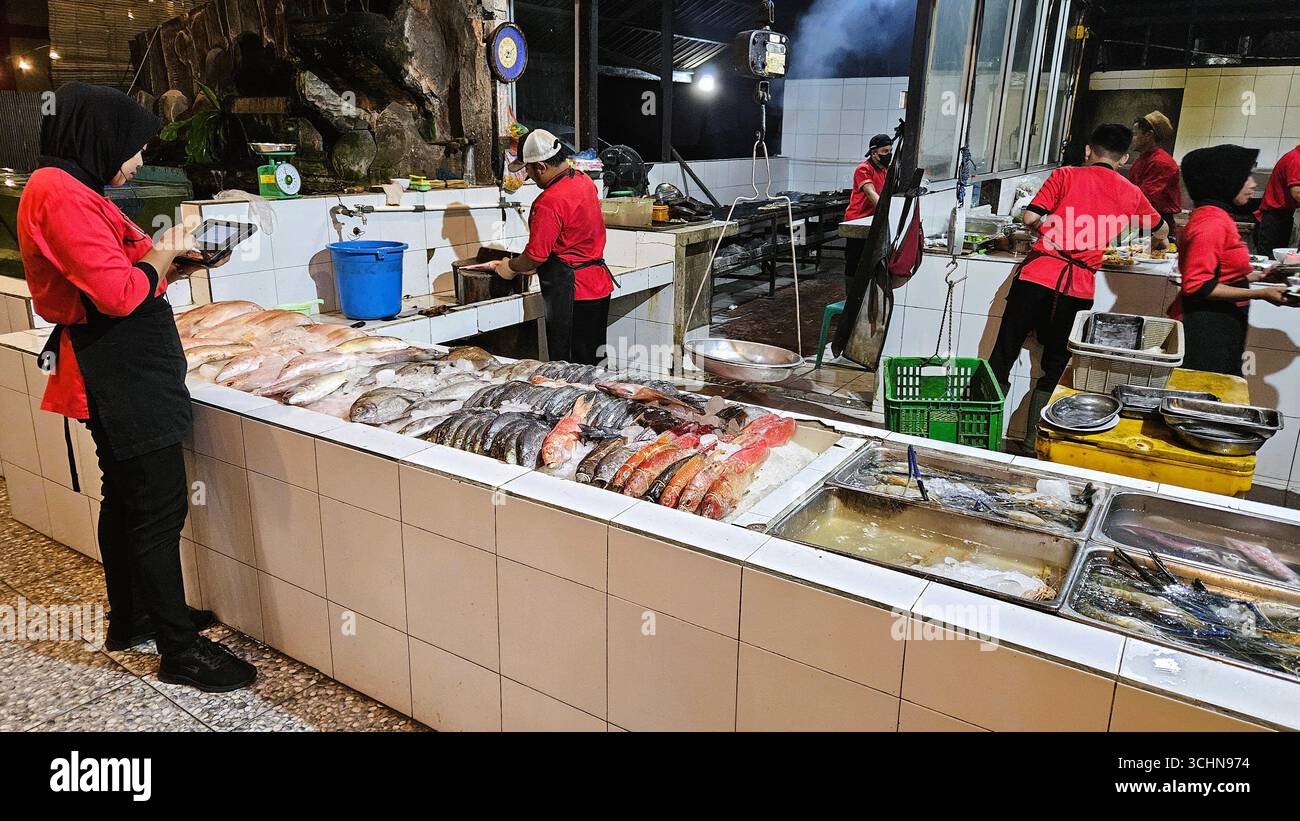 Fish market stall with female vendors in red uniforms selling fresh seafood products. Balikpapan, Indonesia - January 8th, 2024 - Smartphone Captured Stock Image
