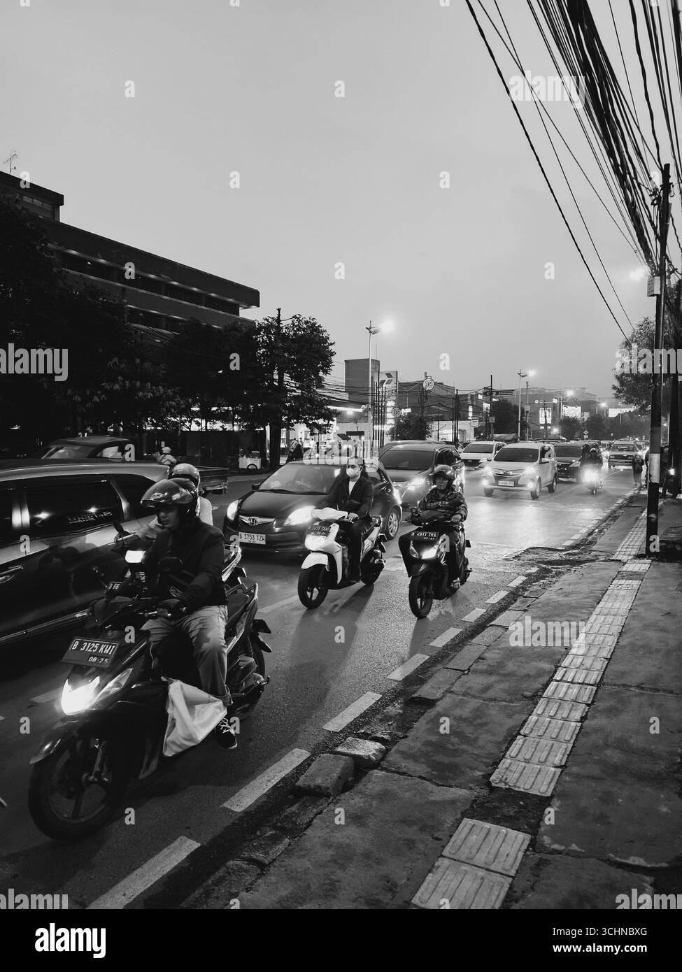 Black and white street view with motorcycles on wet city road during rainy evening. Jakarta, Indonesia - April 1st, 2024 - Smartphone Captured Stock Image