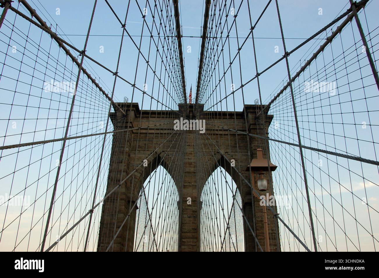 The Brooklyn Bridge photographed from below, showing its stone arches and steel cables stretching into the sky on a clear day in New York City Stock Photo
