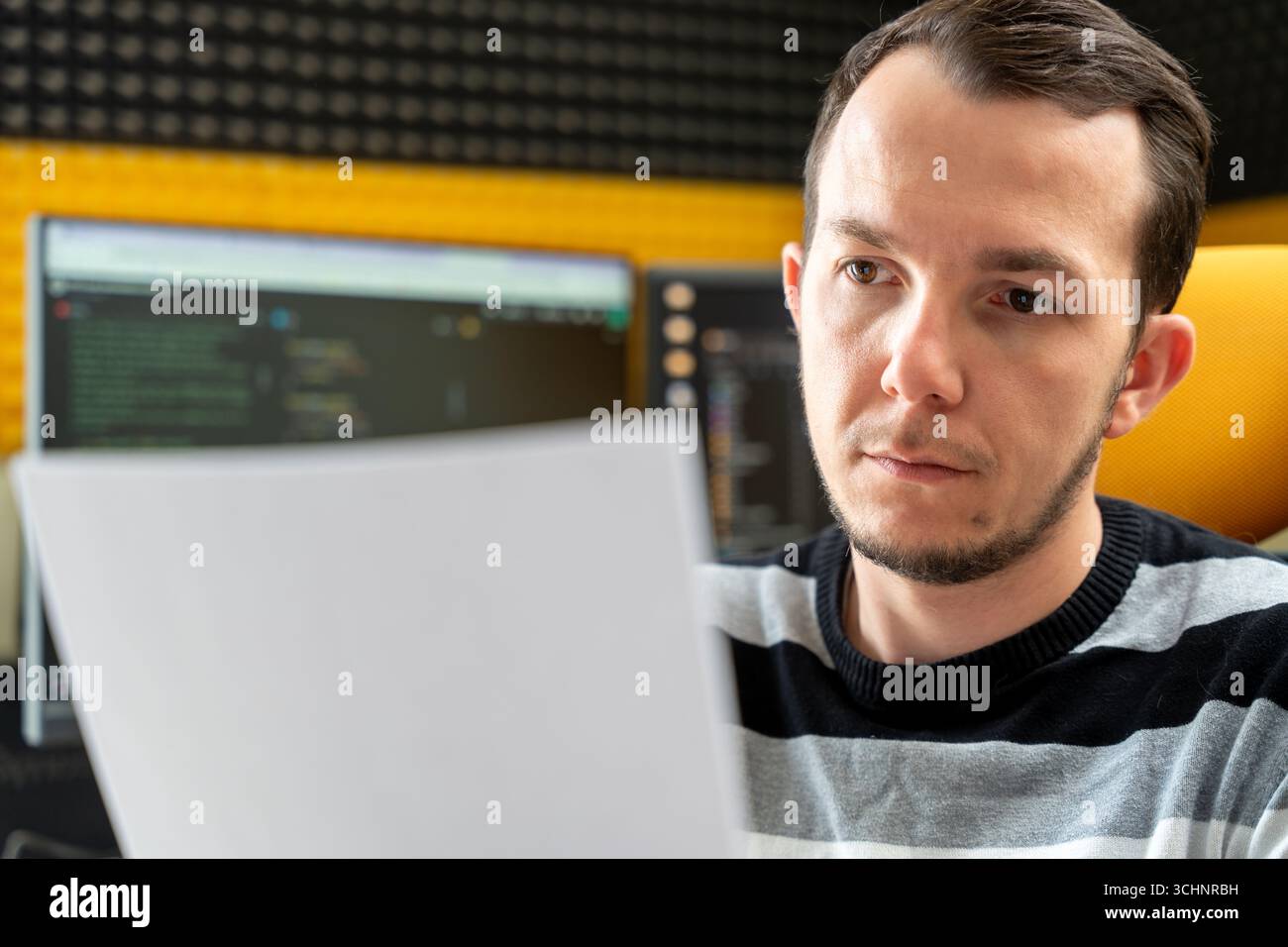 Programmer analyzing printed material with code on screens behind, conveying review and planning phase of software project Stock Photo