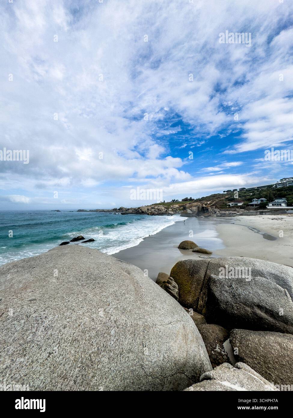 A low-angle, wide-angle shot of a rocky beach in Cape Town. The photograph highlights the pristine, clear water flowing over the sand and rocks in the - Smartphone Captured Stock Image