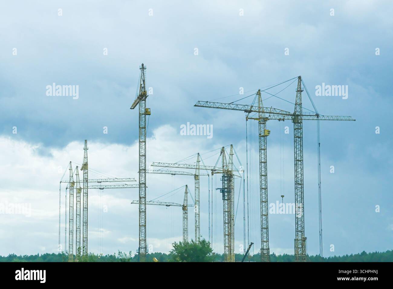Moscow, Russia, 18.08.2025 Many yellow construction tower cranes stand tall against a cloudy sky. Industrial construction site for urban development p Stock Photo