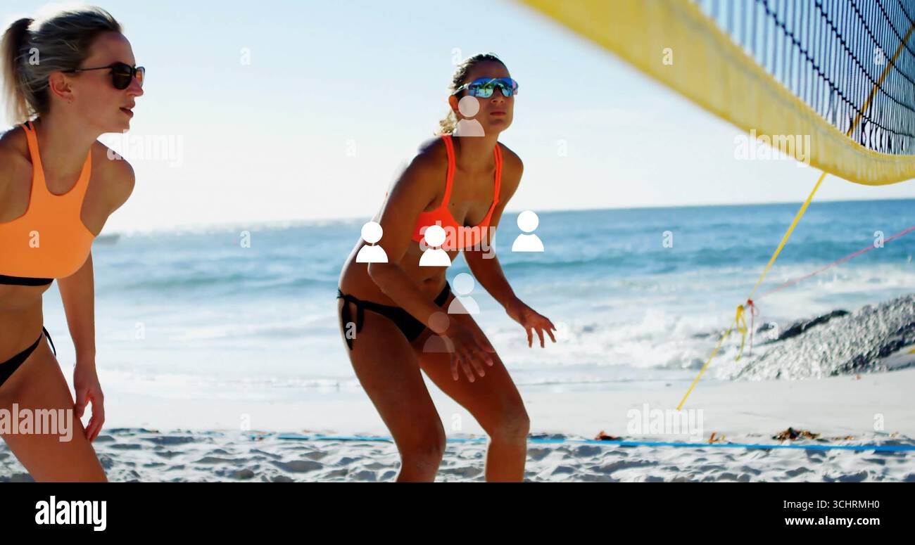 Bracing athlete in orange bikini and shades crouching on beach court, with yellow net, ocean waves Stock Photo