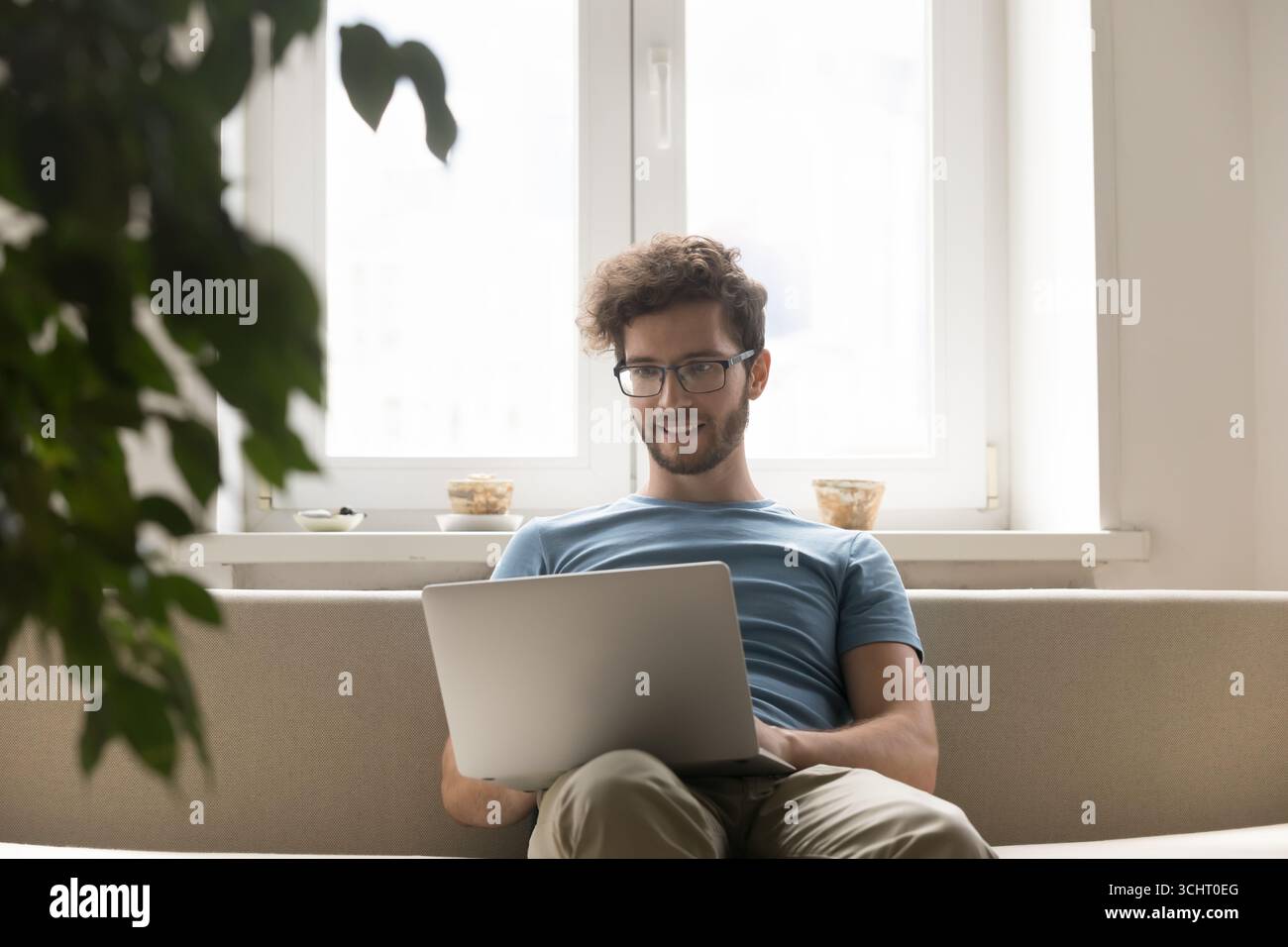 Smiling young guy using notebook on sofa in living room Stock Photo