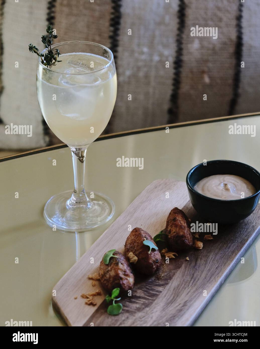 A gourmet drink and appetizer pairing on a modern table setting. The composition features a clear cocktail in a stemmed glass with ice Stock Photo