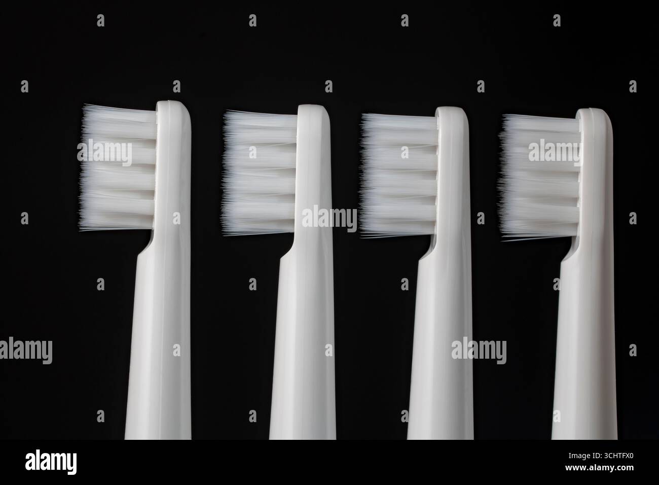 Four white plastic toothbrushes on a black background, close up Stock Photo