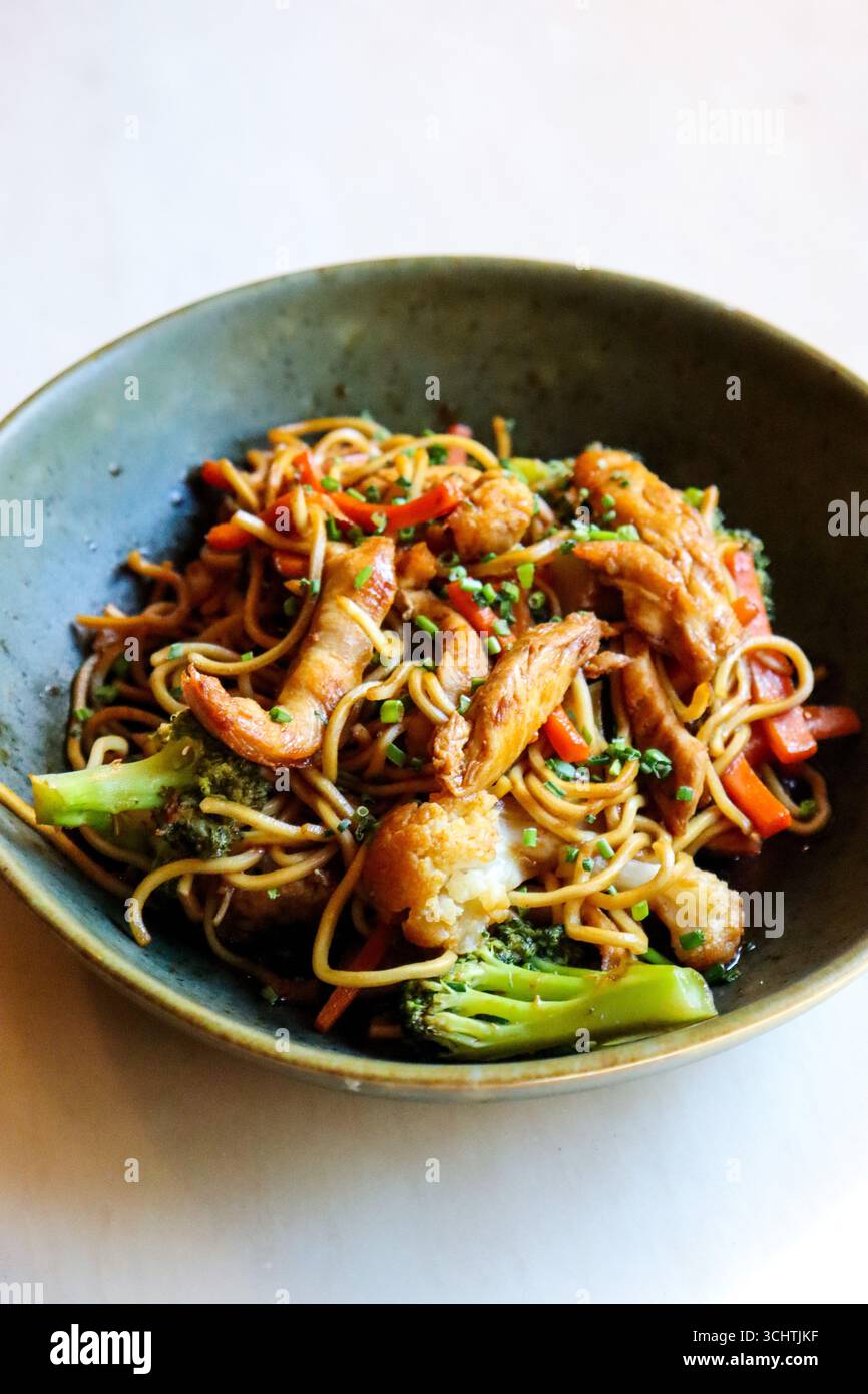 close-up shot of a plate of chicken chow mein. The image showcases tender strips of chicken, an array of colorful, crisp-tender vegetables like bright Stock Photo