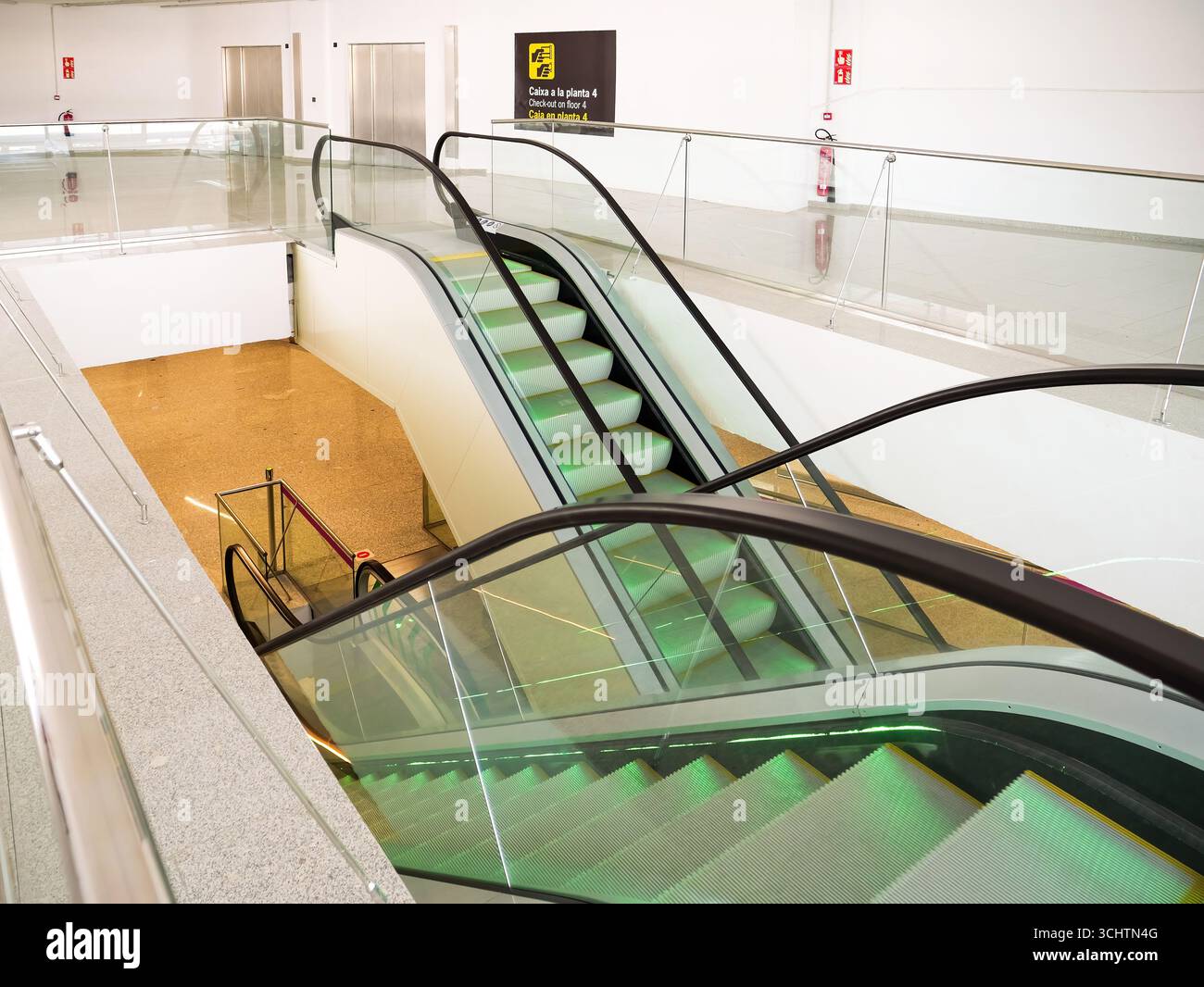 Multiple escalators connect different airport floors with glass railings, yellow floor below, and empty bright modern architecture Stock Photo