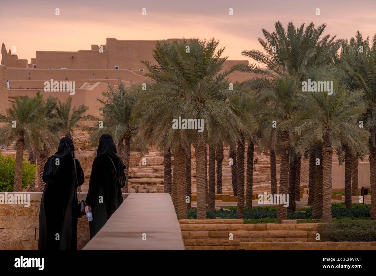 Two Saudi women in Diriyah courtyard, wearing traditional abayas and hijabs, among restored Najdi mudbrick architecture. Stock Photo