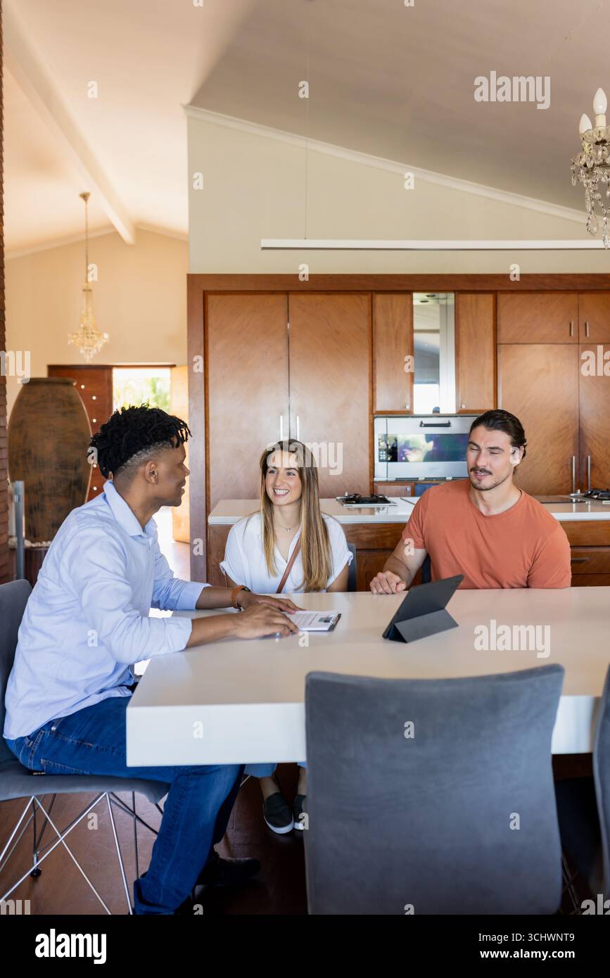 Diverse friends discussing project at home, using tablet and documents on table Stock Photo