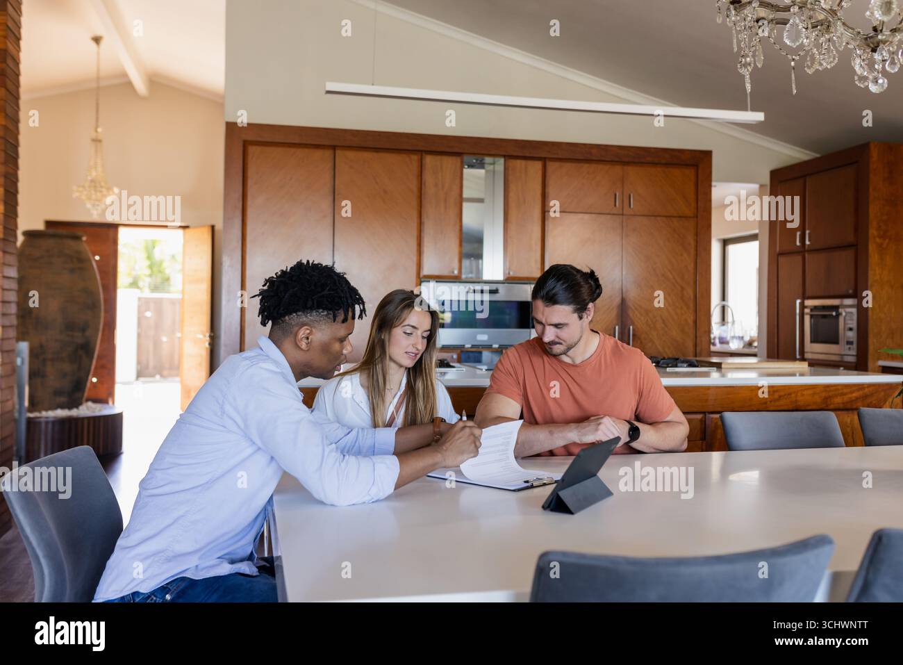 Diverse friends discussing project at home, using tablet and notebook on table Stock Photo
