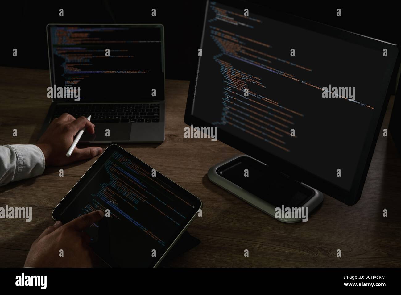 Programmer pointing at laptop screen with visible lines of code and tablet beside, concept of coding, software development, IT, cybersecurity, and dig Stock Photo