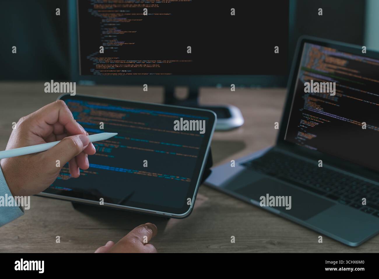 Close-up of programmer freelance working on tablet and laptop with code on screen, modern software development, coding, and remote work in home office Stock Photo